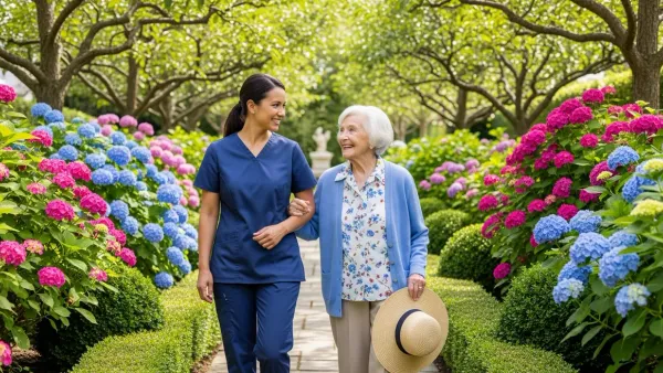 An EagleWings caregiver walks arm-in-arm with a senior client past flowering hydrangeas in a private Baltimore garden.